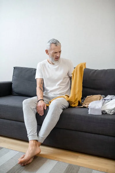 Un hombre de pelo gris que parece infeliz mientras piensa en lavar la ropa — Foto de Stock