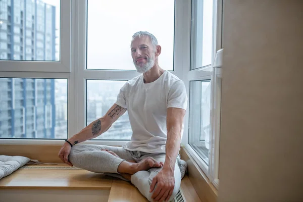 Dospělý muž v bílém tričku dělá jógu a vypadá soustředěně — Stock fotografie