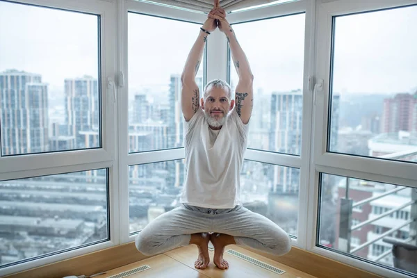 Un hombre maduro en una camiseta blanca haciendo yoga y buscando concentrado — Foto de Stock