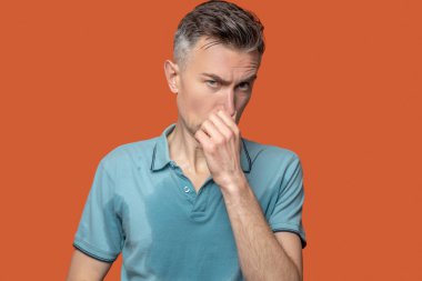 Islak noktalı tişörtlü adam burnuna dokunuyor.