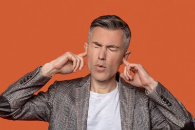 Gözleri sarkmış, kulakları parmaklarıyla kapatan bir adam.