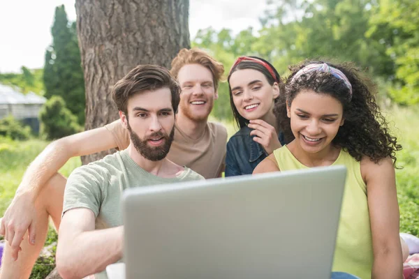 Vier junge glückliche Freunde schauen auf Laptop — Stockfoto