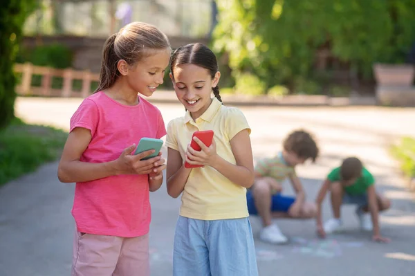 Dziewczyny ze smartfonami i chłopcami za plecami — Zdjęcie stockowe