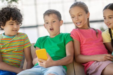 Akıllı telefonu ve arkadaşları olan şaşkın bir çocuk.