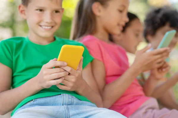 Niño alegre con smartphone amarillo y amigos —  Fotos de Stock