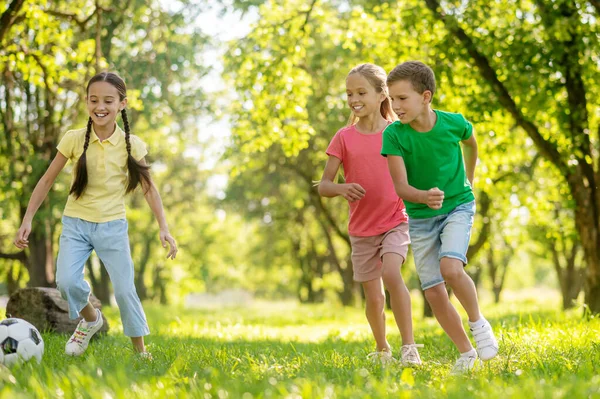 Dos chicas sonrientes y niño alegre persiguiendo pelota — Foto de Stock