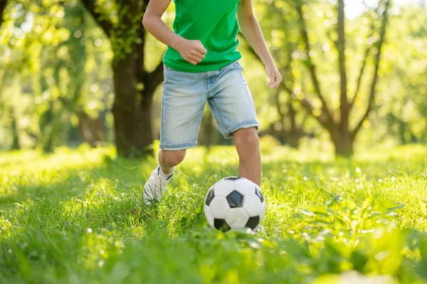Criança júnior jogando futebol no gramado verde — Fotografia de Stock