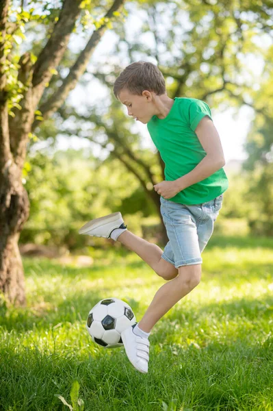 Menino pulando com bola de futebol na natureza — Fotografia de Stock