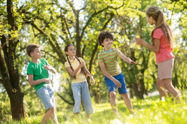 Meninos e meninas alegres com bolhas de sabão no parque — Fotografia de Stock