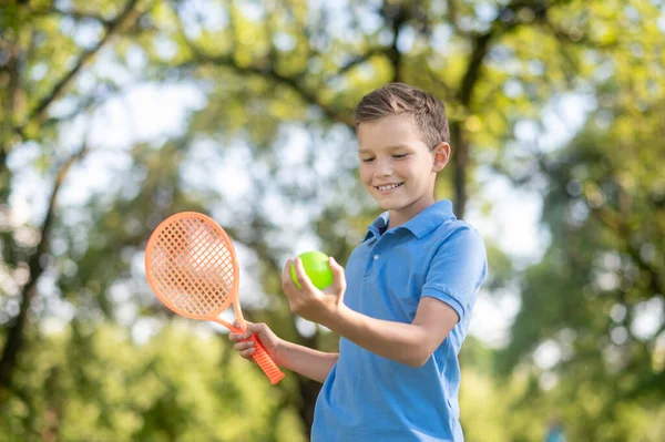 Smiling boy looking at tennis ball in hand — Stock Photo, Image