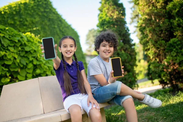 Χαμογελώντας αγόρι και κορίτσι δείχνει smartphones — Φωτογραφία Αρχείου