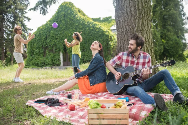 Ragazzo con ragazza seduta su plaid e amici dietro — Foto Stock