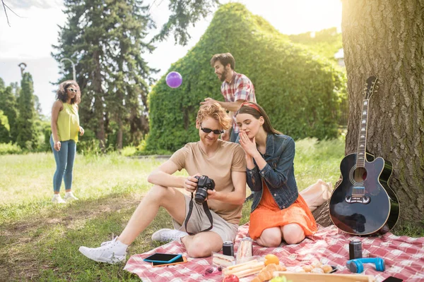 Cara e namorada olhando fotos e amigos atrás — Fotografia de Stock