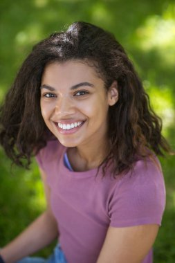 Tatlı, esmer, genç bir kız gülümsüyor.