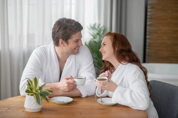 Ett par i vita badrockar som dricker kaffe och känner sig glada — Stockfoto