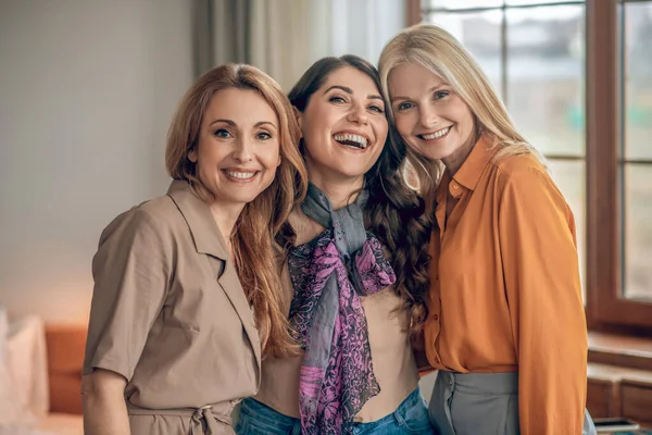 Три женщины в элегантных нарядах улыбаются и выглядят счастливыми — стоковое фото