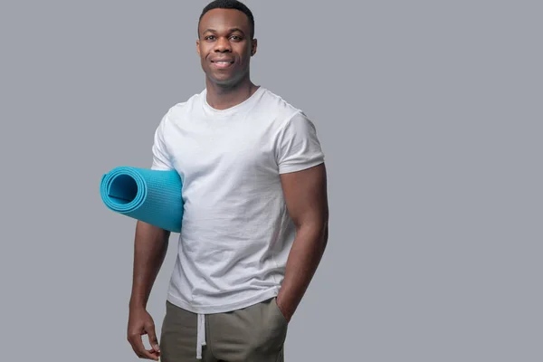 Un hombre con una camiseta blanca con una esterilla azul en las manos — Foto de Stock