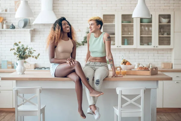 Two young adult women sitting on kitchen table — Foto Stock