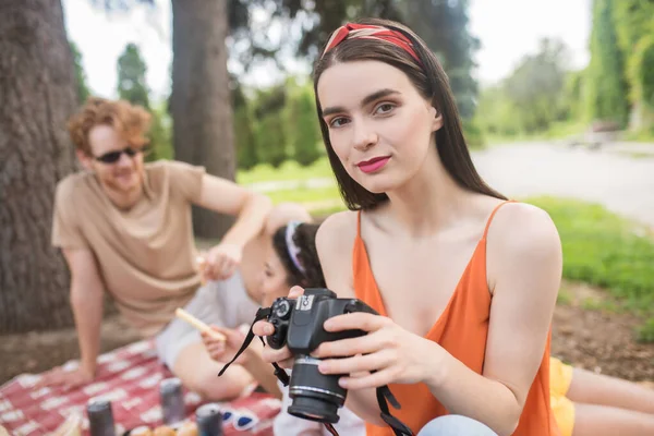 Roztomilá dívka s kamerou a přáteli za zády — Stock fotografie