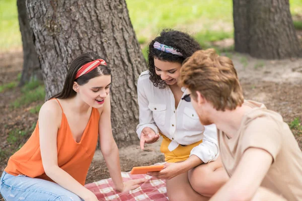 Två tjejer och kille med surfplatta på picknick — Stockfoto