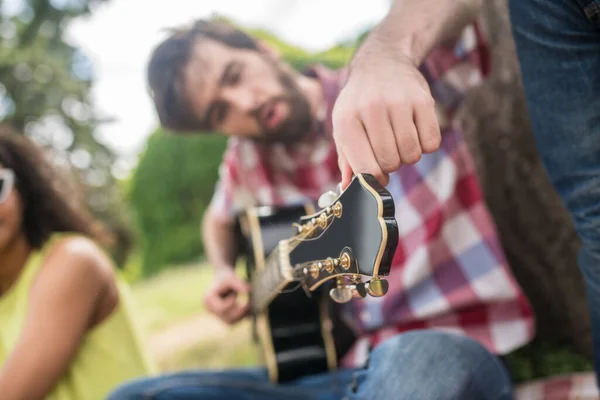 Guy fixeert snaren op gitaar tijdens de picknick — Stockfoto
