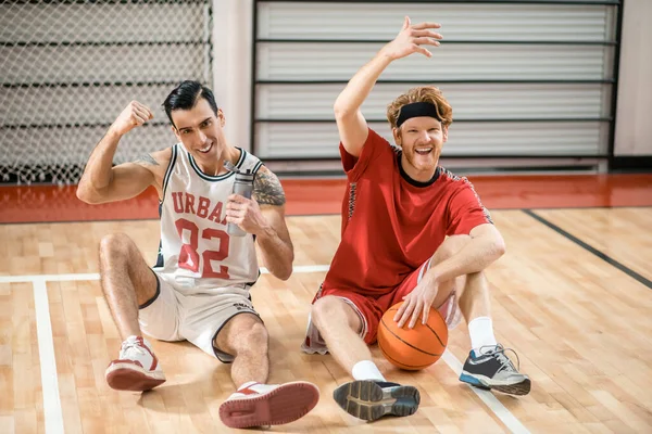 Two friends sitting on the floor in the gym and resting after the game — Stock Photo, Image