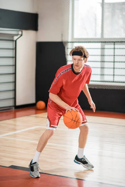 Homem de gengibre em um sportswear vermelho jogando basquete — Fotografia de Stock