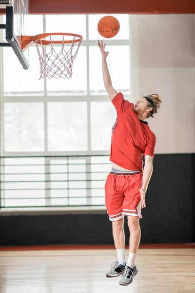 Ingefära man i en röd sportkläder kasta bollen i korgen — Stockfoto