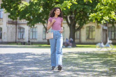 Kot pantolon ve pembe tişörtle parkta gülümseyen tatlı mulatta.
