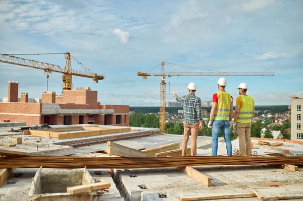 Tre män i skyddshjälmar inspekterar byggarbetsplatsen — Stockfoto