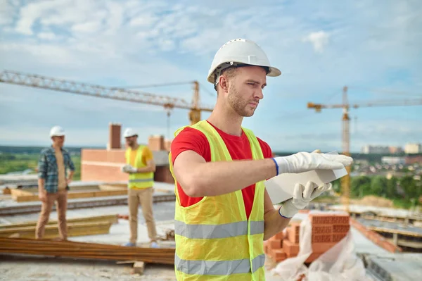 Ladrillo serio en un hardhat que prueba la calidad del material de construcción —  Fotos de Stock