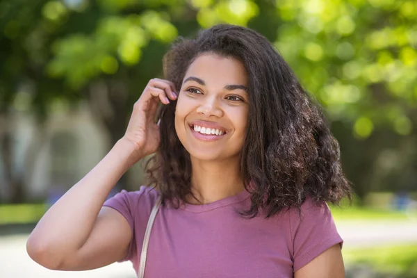 Lachende schattige mulatta in jeans en roze tshirt in het park — Stockfoto