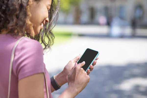 Ganska leende mulatta med en smartphone ser haft och glad — Stockfoto