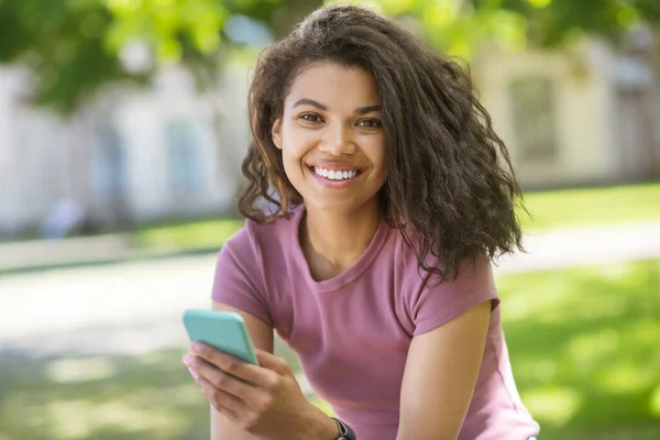 A cute girl in a pink tshirt spending time in the park and chatting online — Foto Stock