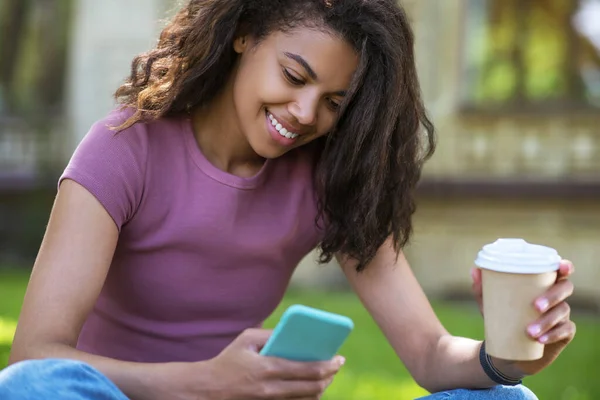 Una linda chica con una camiseta rosa sentada en la hierba y tomando café — Foto de Stock