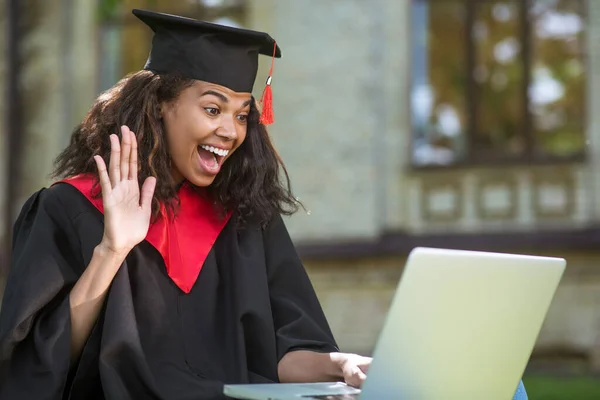 Um graduado bonito em vestido acadêmico ter uma chamada vieo e sentir-se feliz — Fotografia de Stock