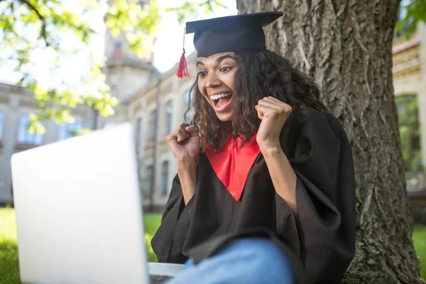 A cute graduate in academic gown having a vieo call and feeling happy — Stock Photo, Image