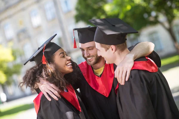 Drie afgestudeerden knuffelen en bespreken hun afstuderen — Stockfoto