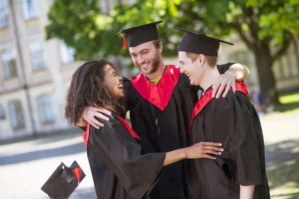 Tres graduados abrazando y discutiendo su graduación — Foto de Stock