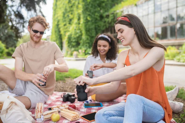 Two girls and guy opening drink at picnic — Foto Stock