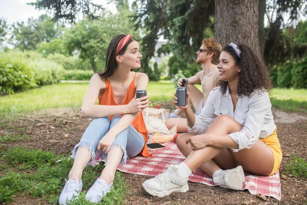 Two girls with drink and guy behind in nature — Foto Stock