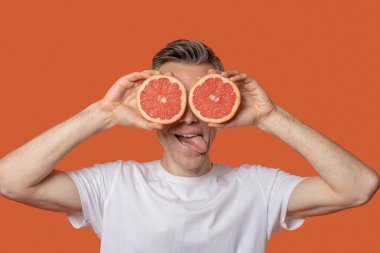 Göz hizasında greyfurt parçaları tutan bir adam.