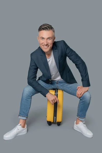 Улыбающийся привлекательный мужчина сидит на чемодане — стоковое фото
