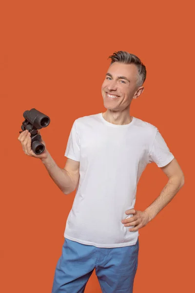 Молодой взрослый улыбающийся мужчина стоит с биноклем — стоковое фото