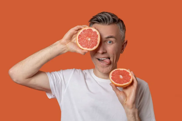 Man showing tongue holding halves of grapefruit — Stock Photo, Image