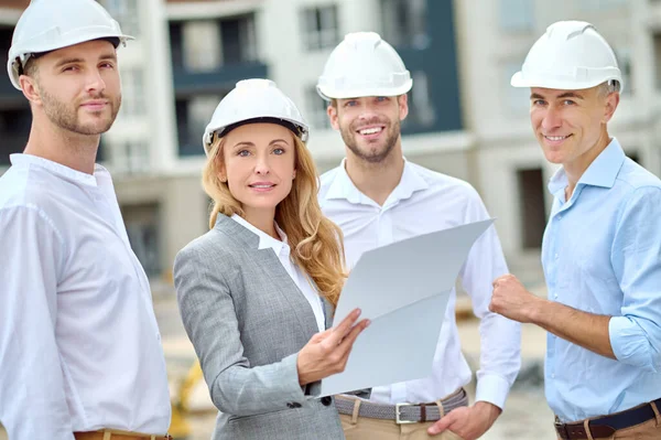 Inspector de construcción seguro con un documento y constructores mirando hacia el futuro —  Fotos de Stock