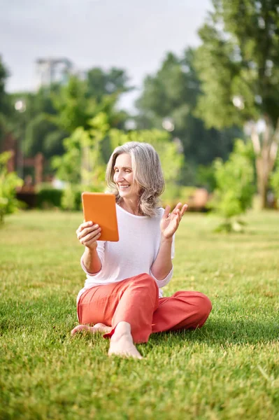 Fröhliche Frau mit Tablet auf Gras sitzend — Stockfoto