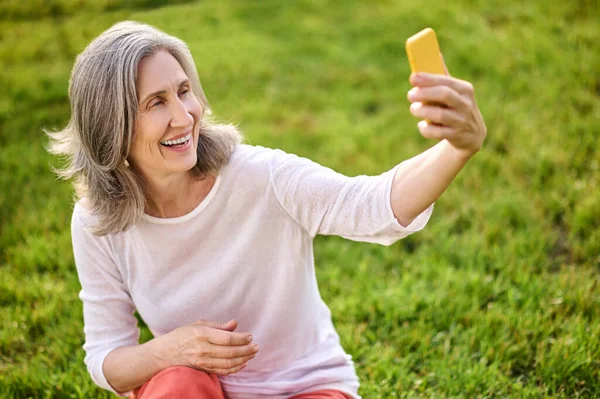 Brillante donna adulta con smartphone in mano tesa — Foto Stock