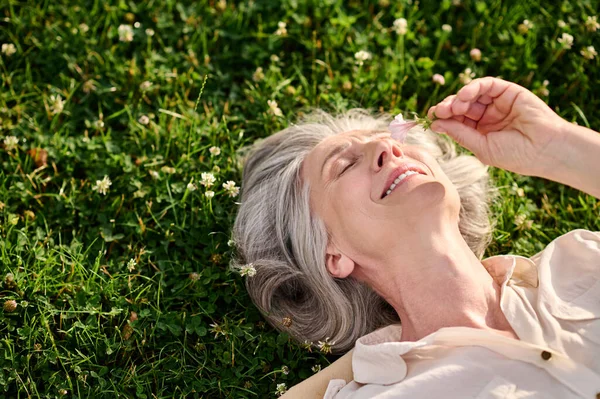 Усміхнена жінка на газоні з квіткою в руці — стокове фото