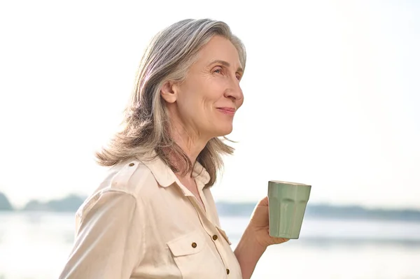 Улыбающаяся женщина с чашкой кофе в природе — стоковое фото